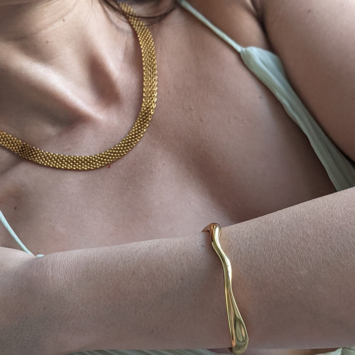 Close-up of a person wearing a gold necklace and bracelet on a neutral background