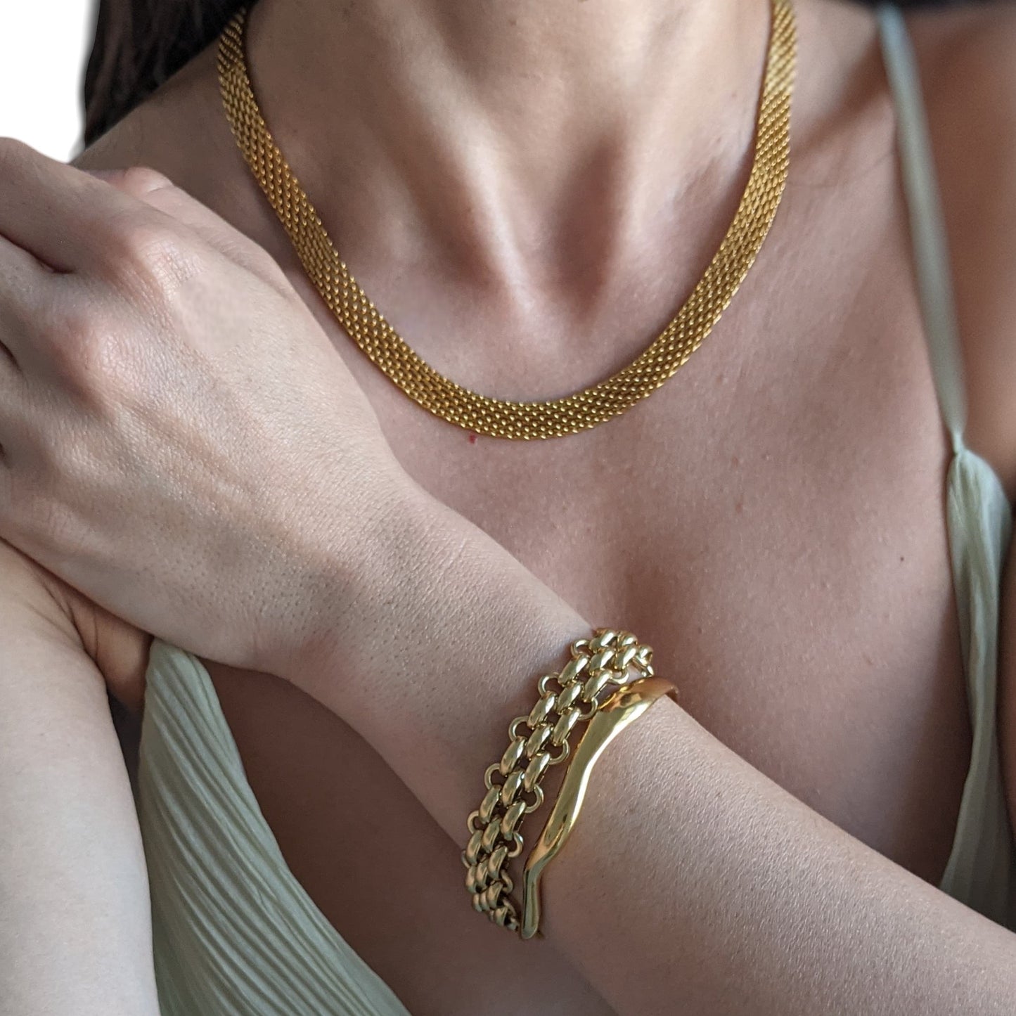 Gold necklace and bracelet on a person's arm with a neutral background