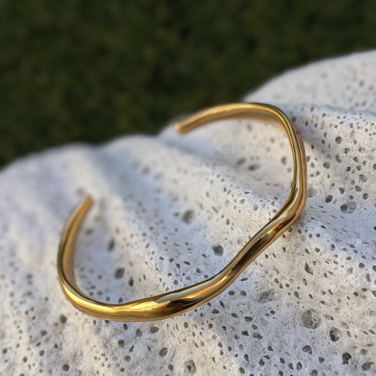 Gold bracelet on a textured stone surface with a blurred natural background