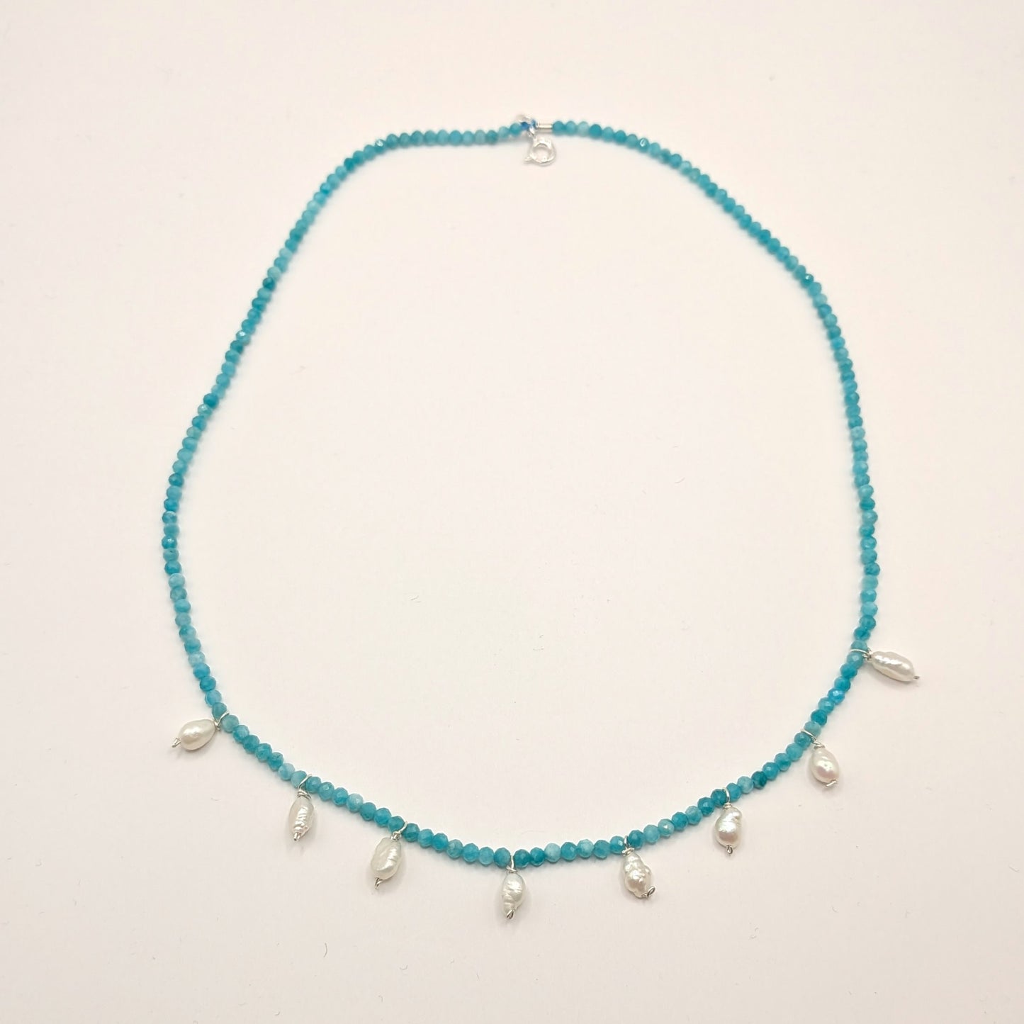 Blue beaded necklace with silver drops on a light beige background
