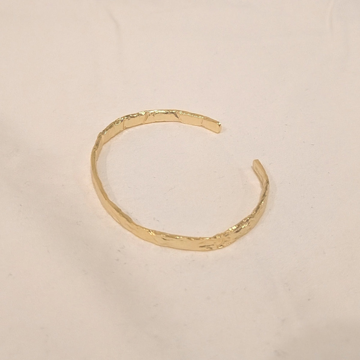A textured gold open cuff bracelet on a plain off-white background.