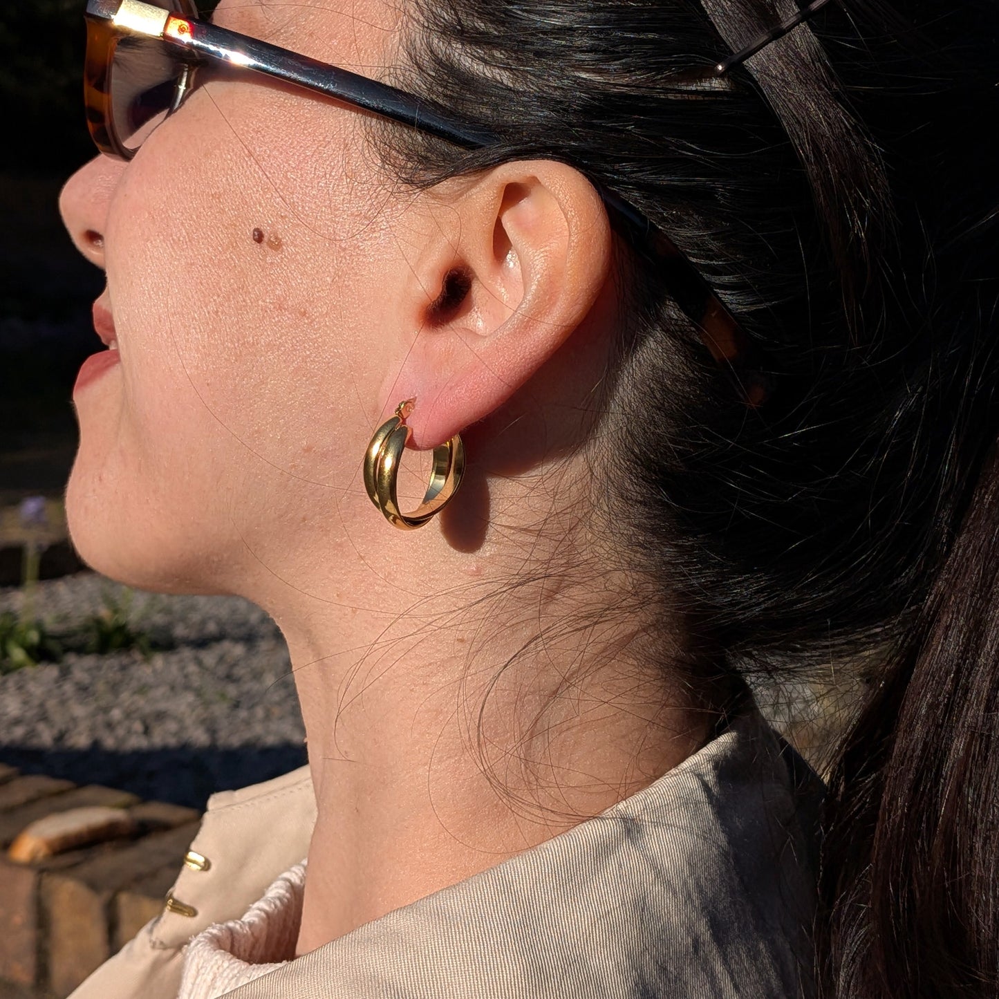 Close-up of a person wearing gold hoop earrings with sunglasses on.