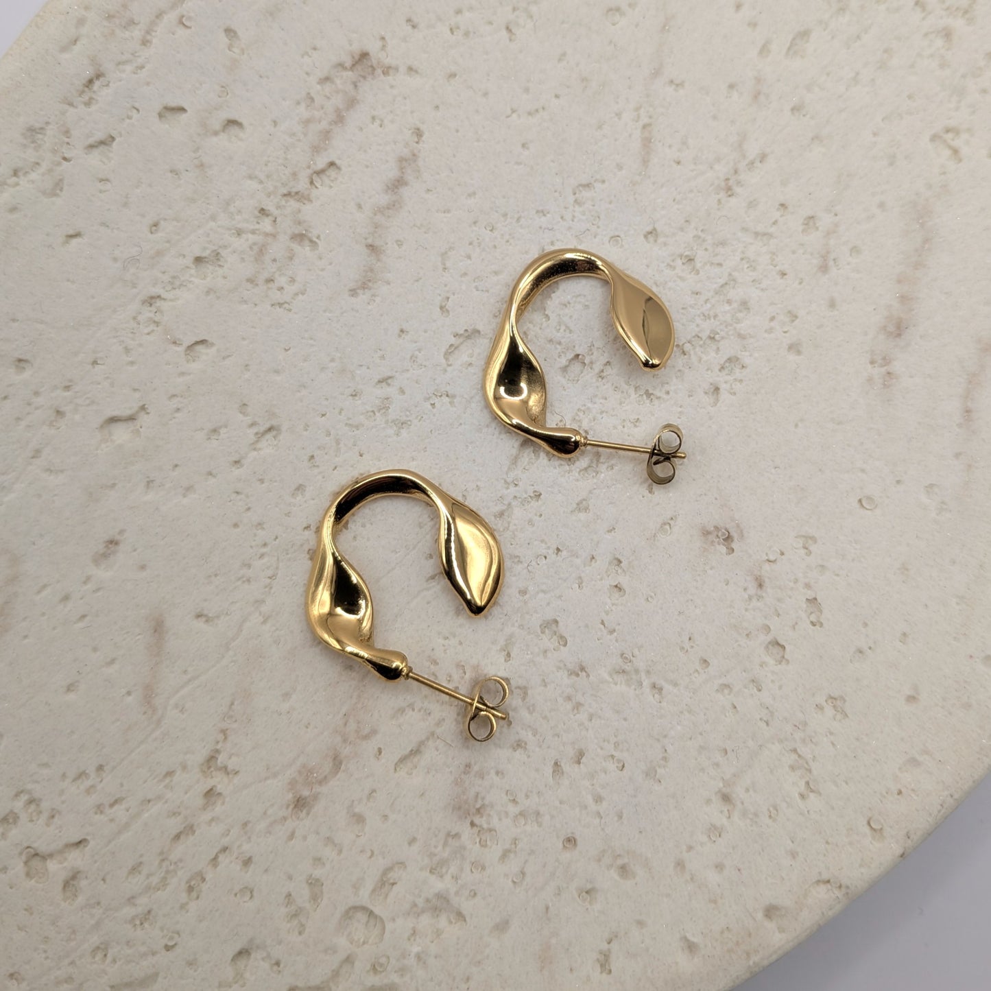 Gold hoop earrings on a beige stone surface