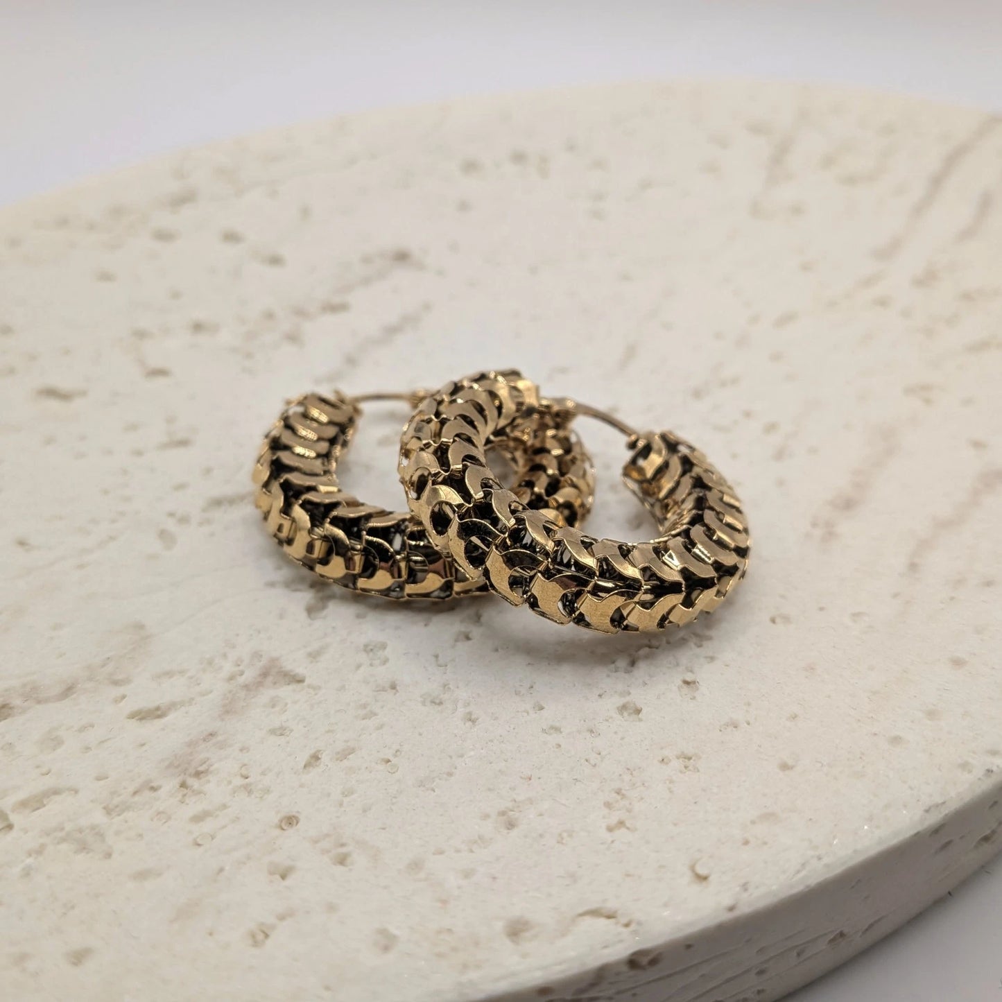 Gold hoop earrings on a textured beige surface