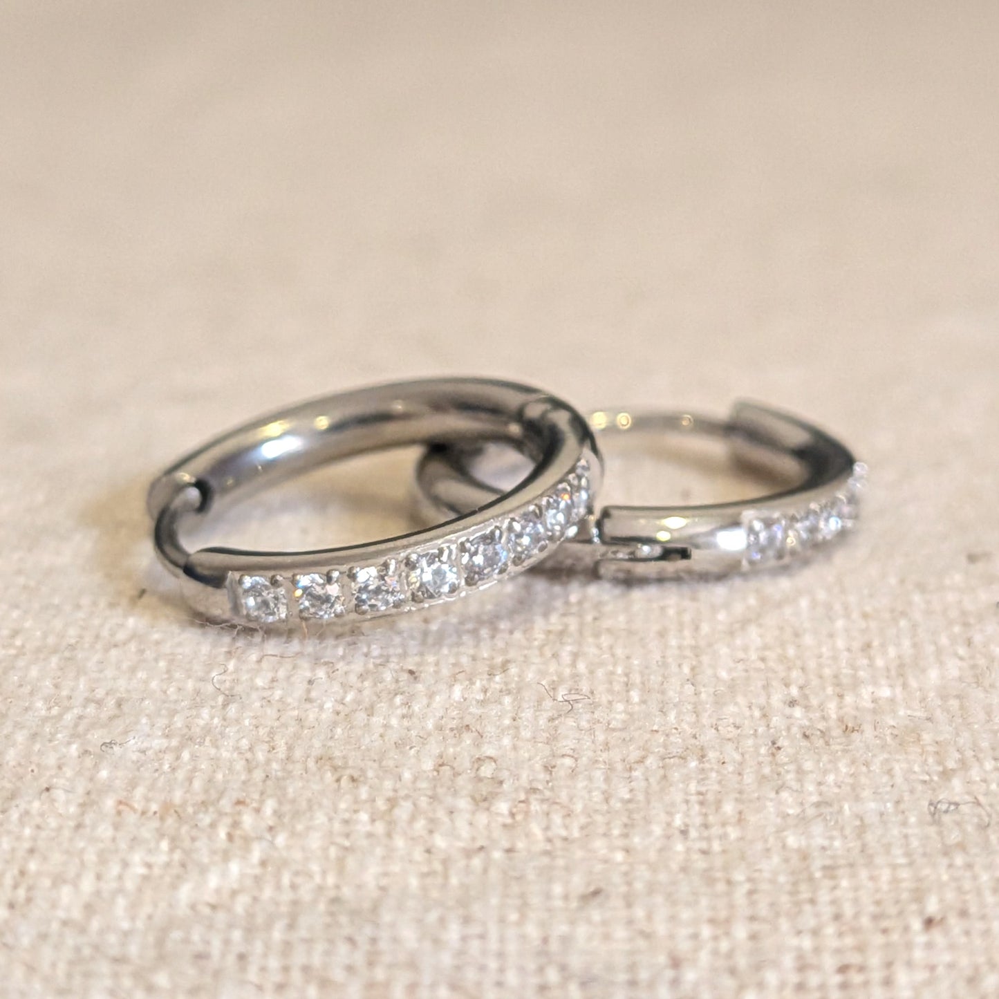 Pair of silver hoop earrings with embedded stones on a beige fabric background