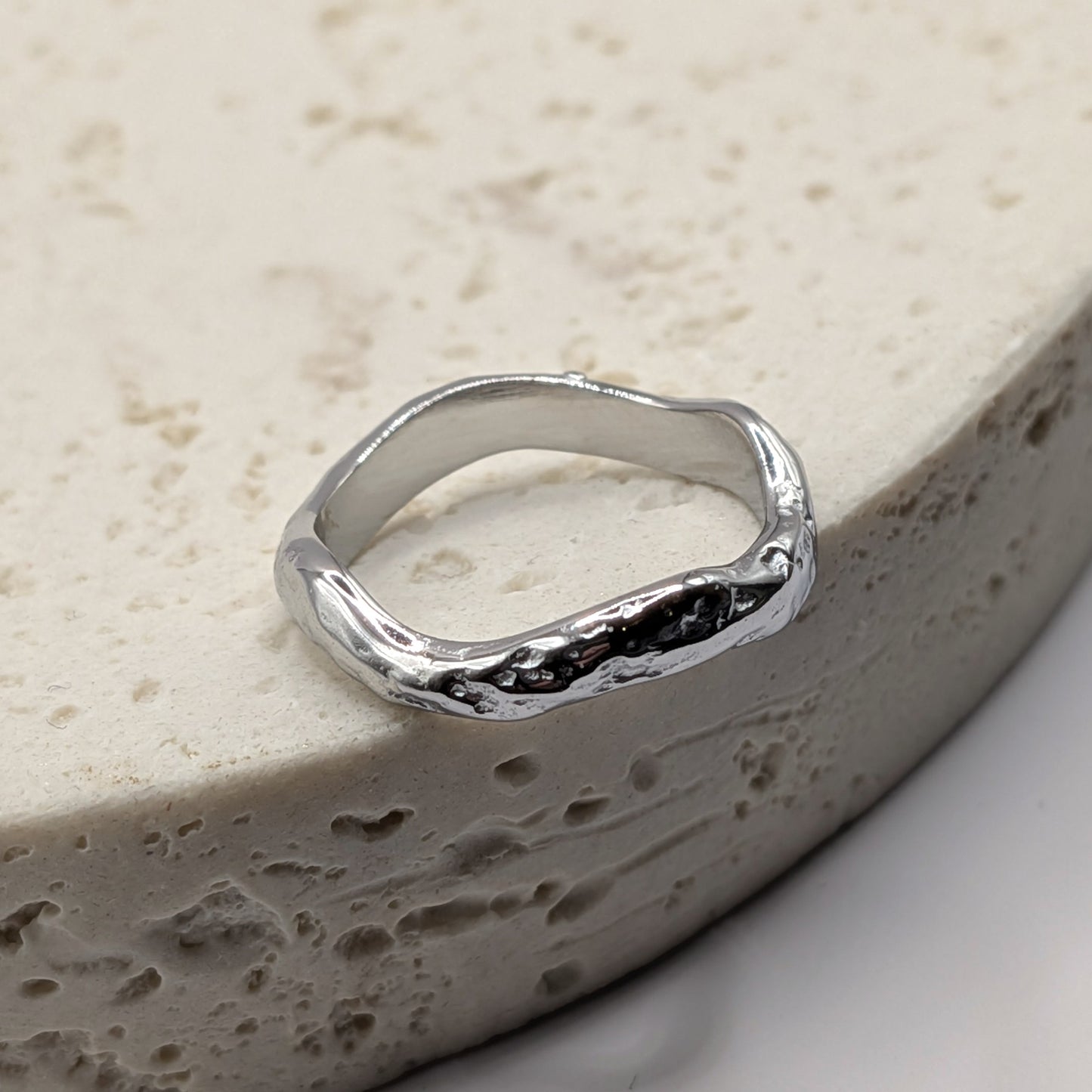 Silver ring with a textured design on a beige stone surface
