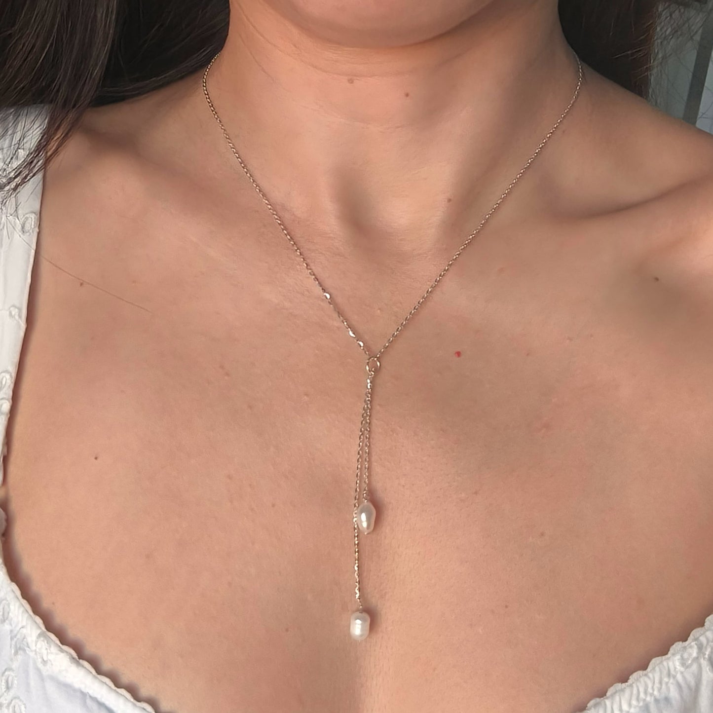 Close-up of a necklace with pearl drops worn by a person.