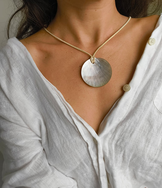 Close-up of a person wearing a necklace with a round pendant on a white shirt.
