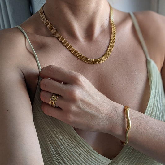Person wearing gold jewelry including a necklace, ring, and bracelet.