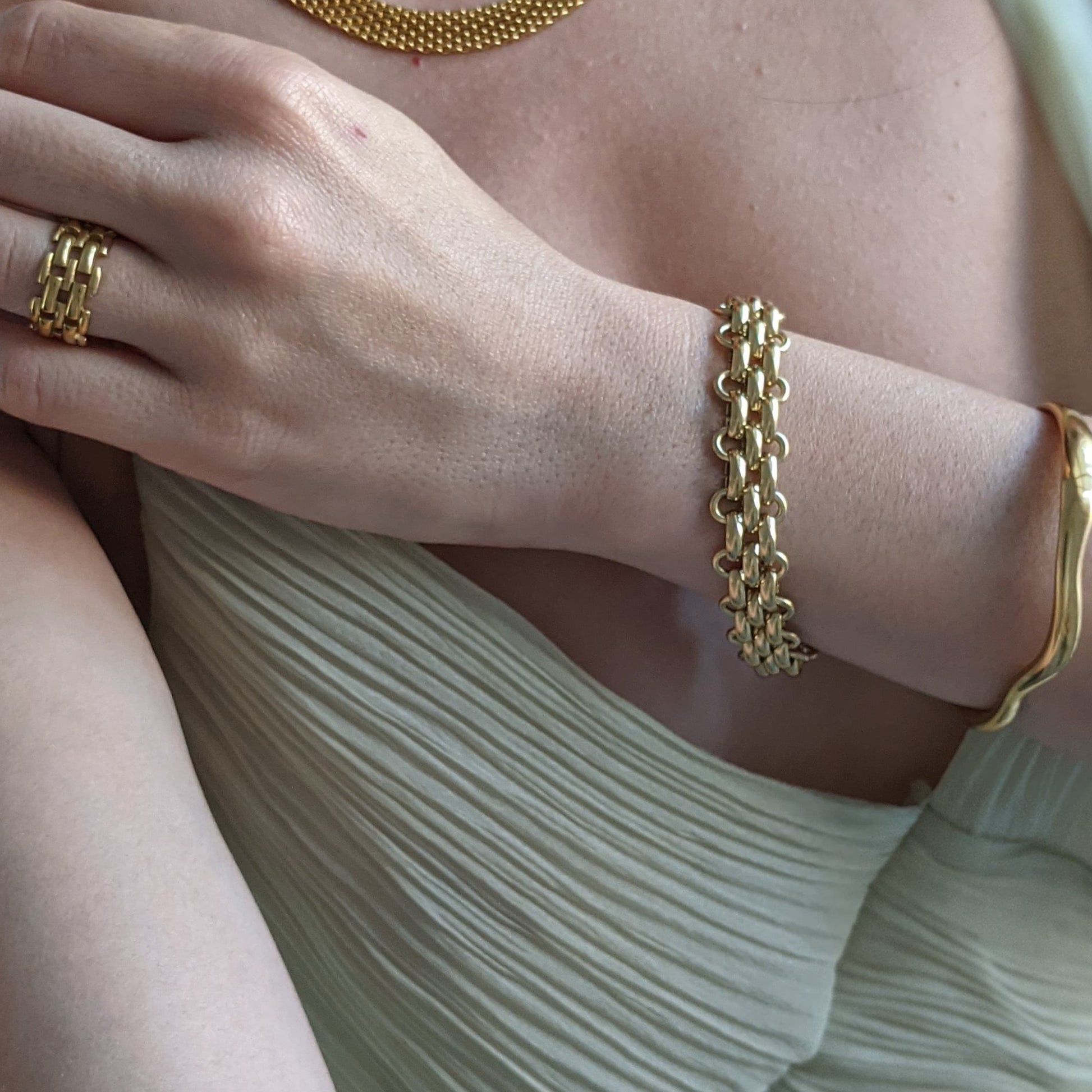 Close-up of a person's wrist wearing a gold bracelet with a neutral background