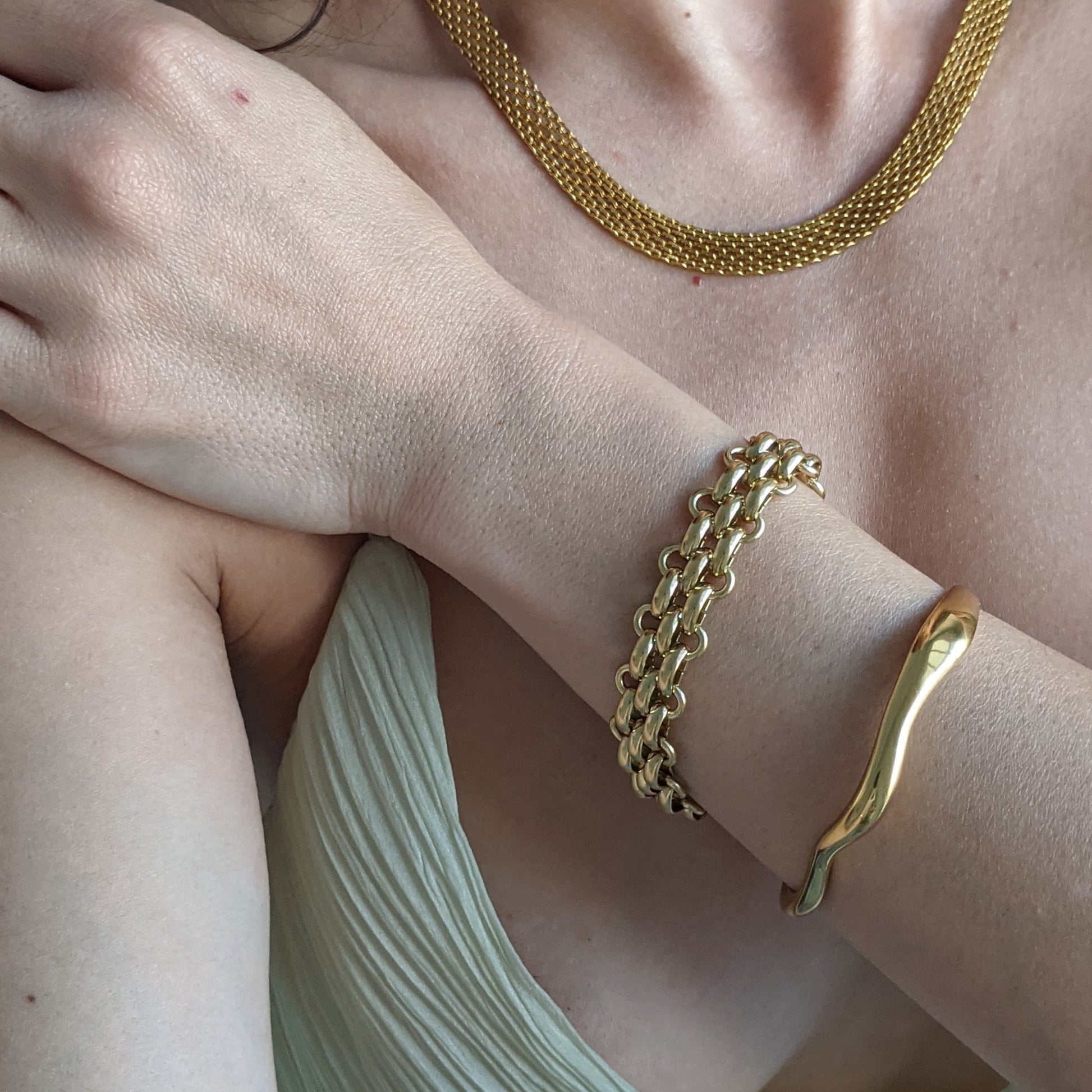 Close-up of a person wearing gold chain jewelry on a light background