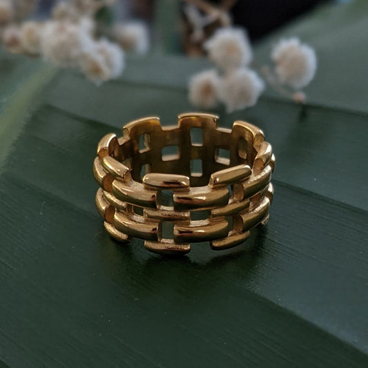Gold woven ring on a dark green surface with blurred white flowers in the background