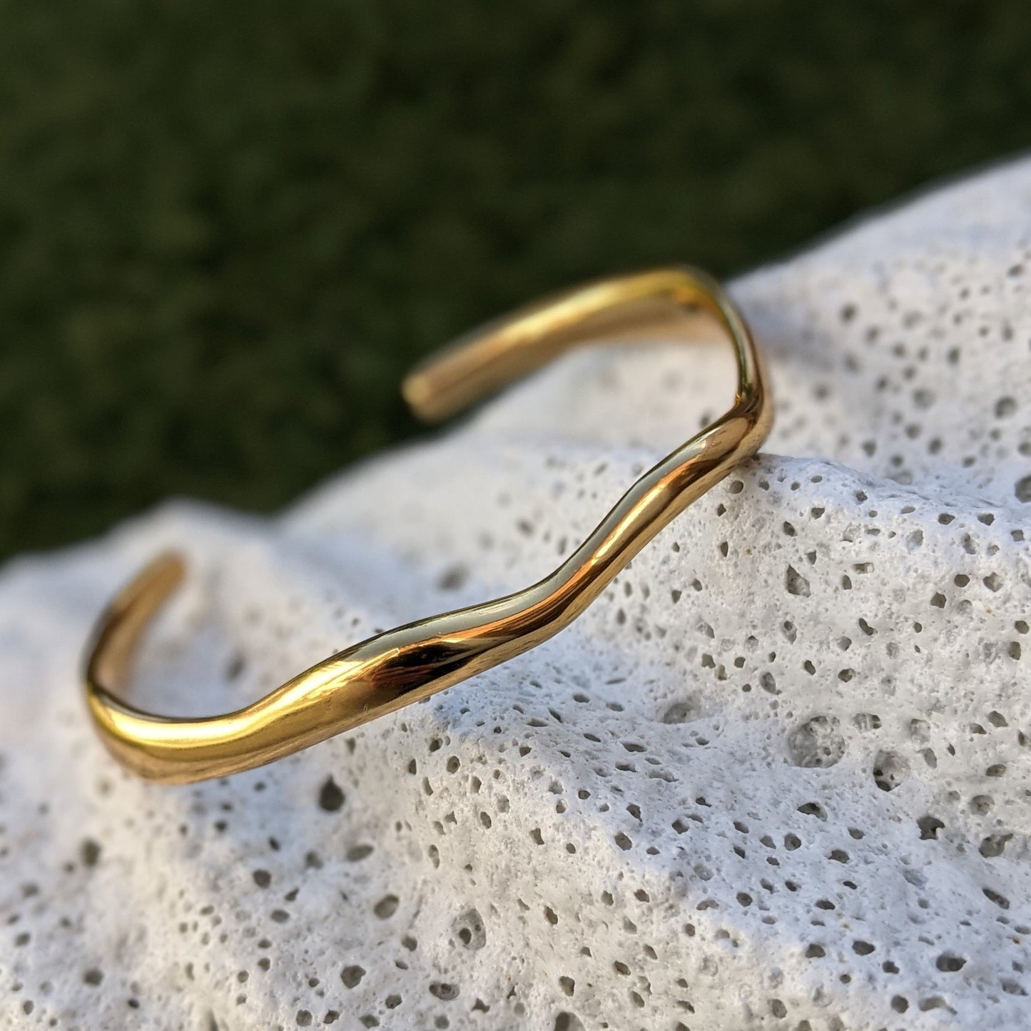 Gold bracelet on a textured stone surface with a blurred green background