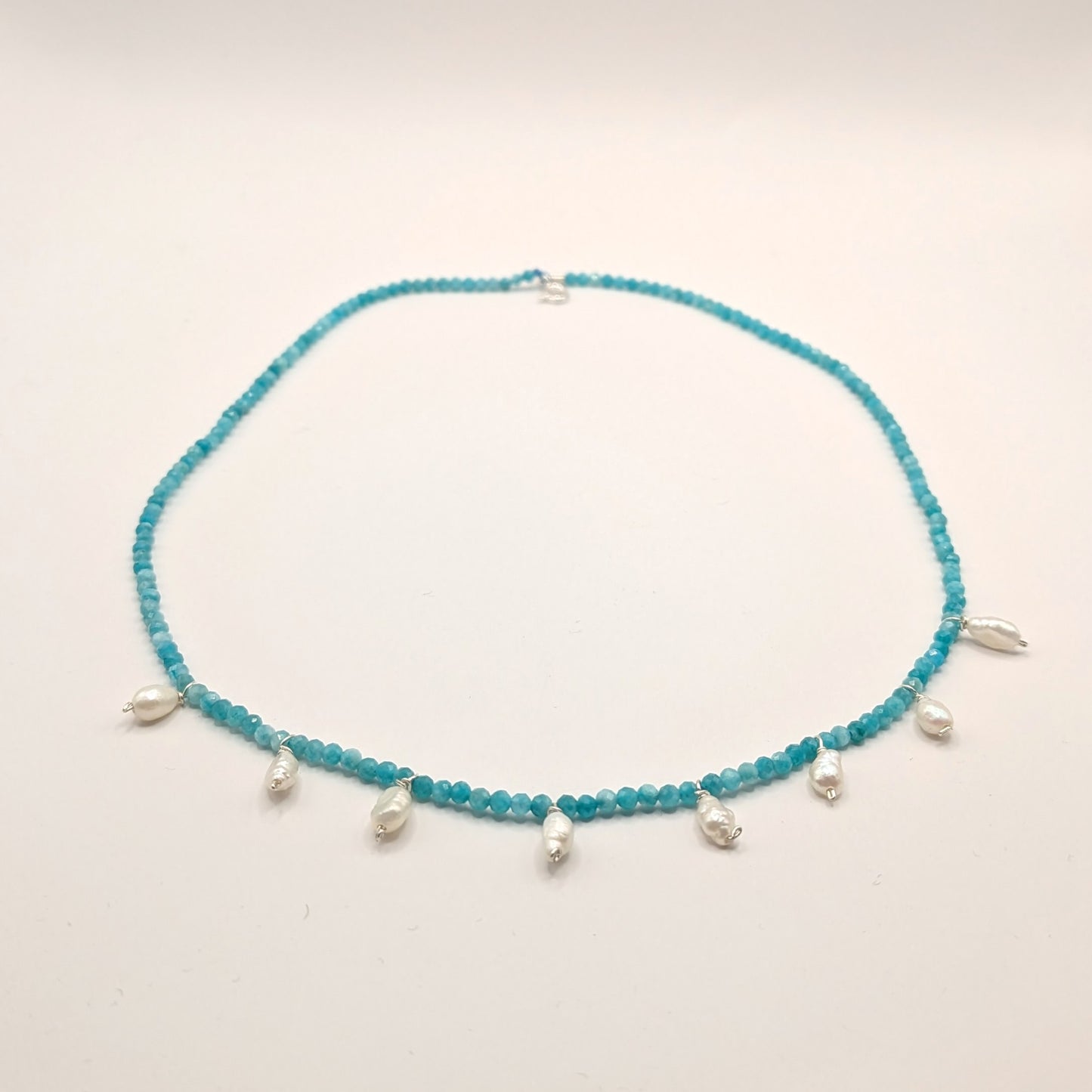 Turquoise beaded necklace with silver charms on a light gray background