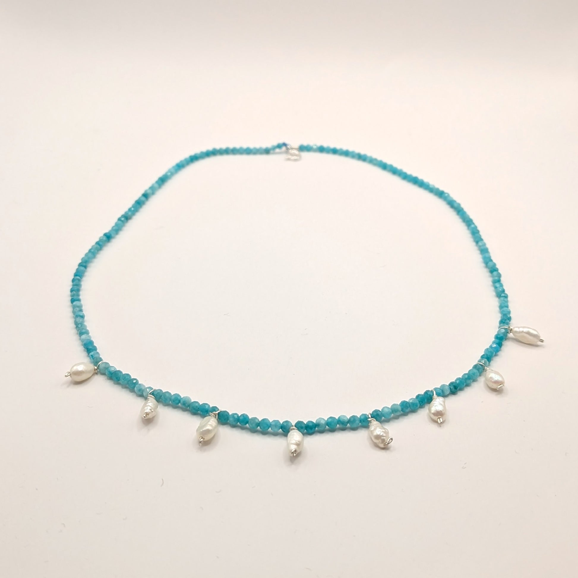 Turquoise beaded necklace with silver charms on a light gray background