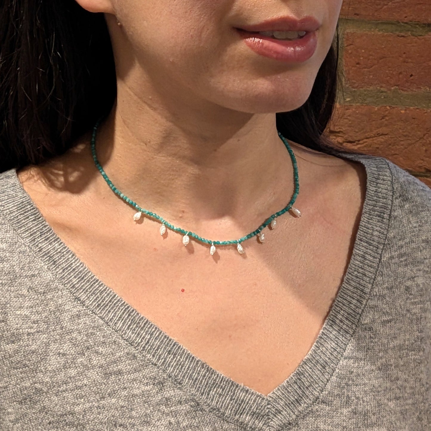 Woman wearing a green beaded necklace against a brick wall.