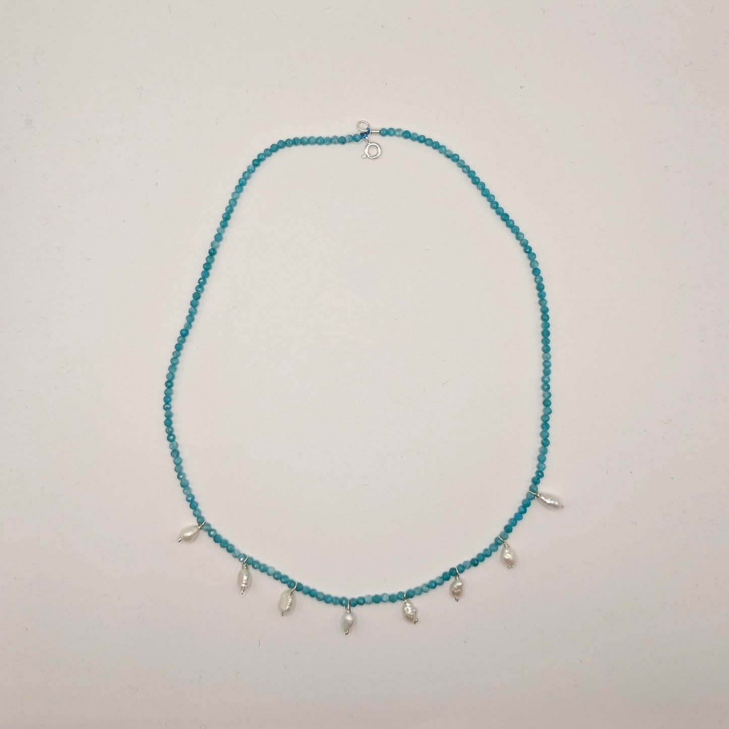 Teal beaded necklace with small silver charms on a light gray background