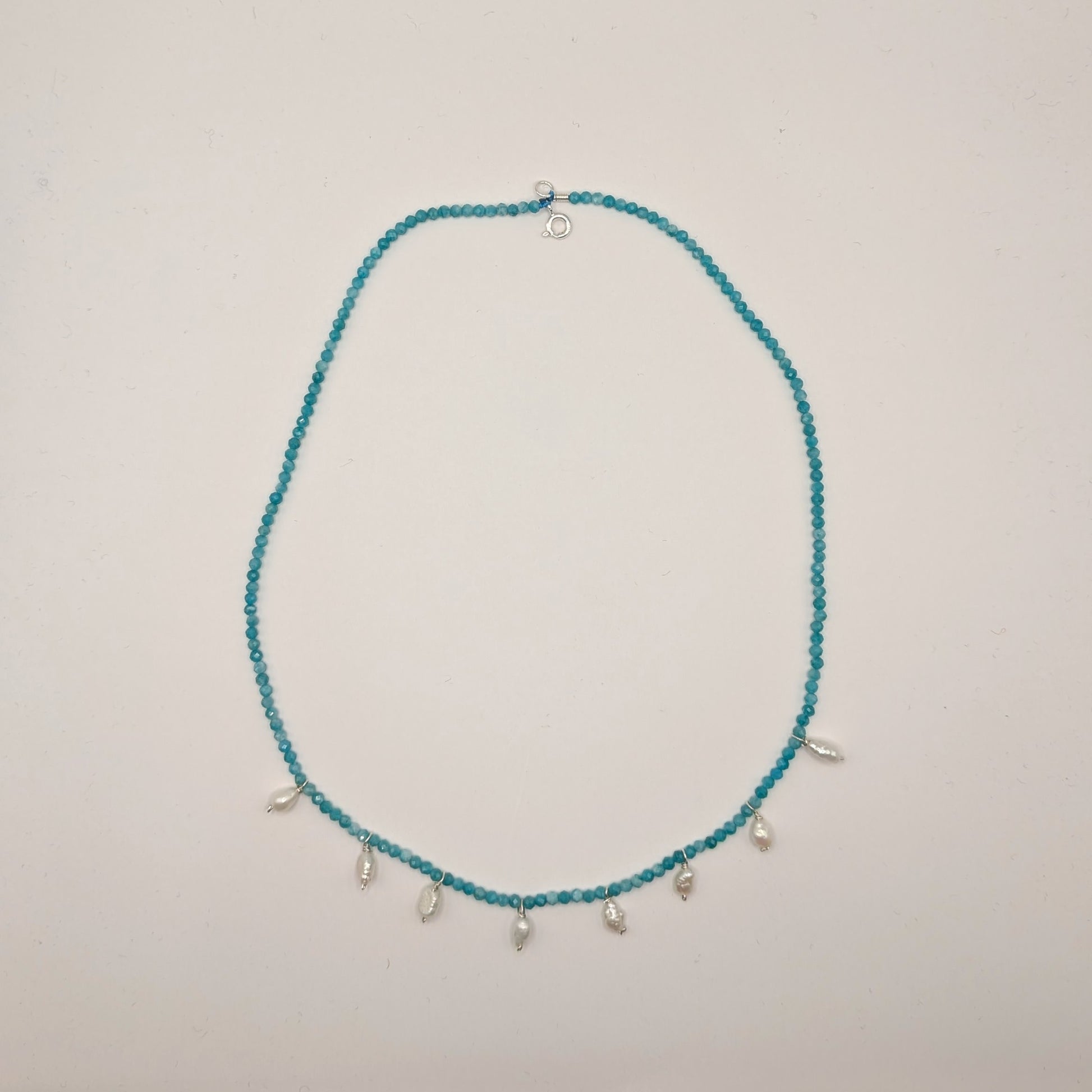 Teal beaded necklace with small silver charms on a light gray background