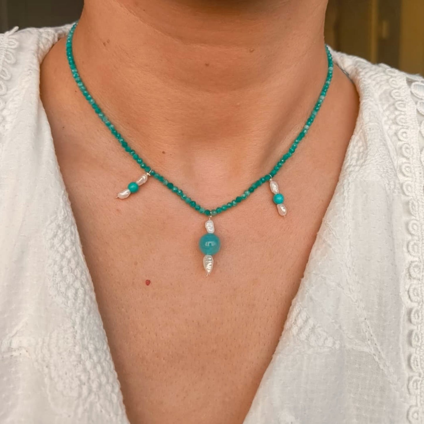 Person wearing a turquoise beaded necklace with white accents