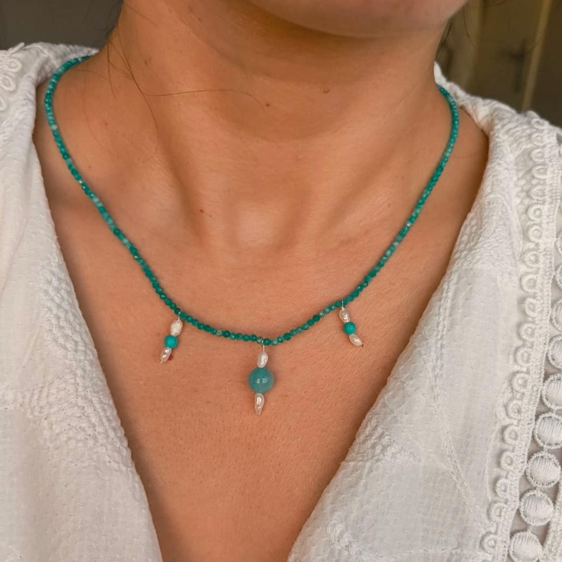 Close-up of a person wearing a green beaded necklace with white accents.