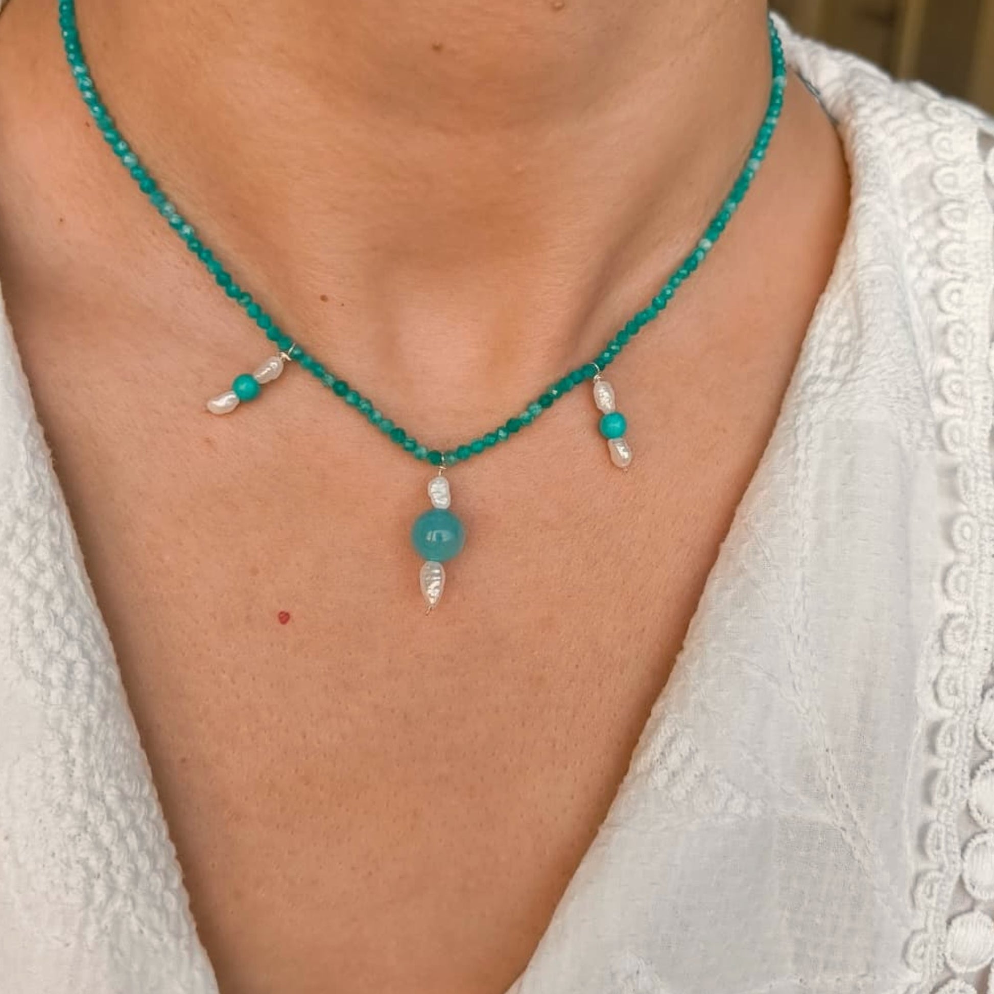 Teal beaded necklace with pearl accents worn by a person in a white lace garment.