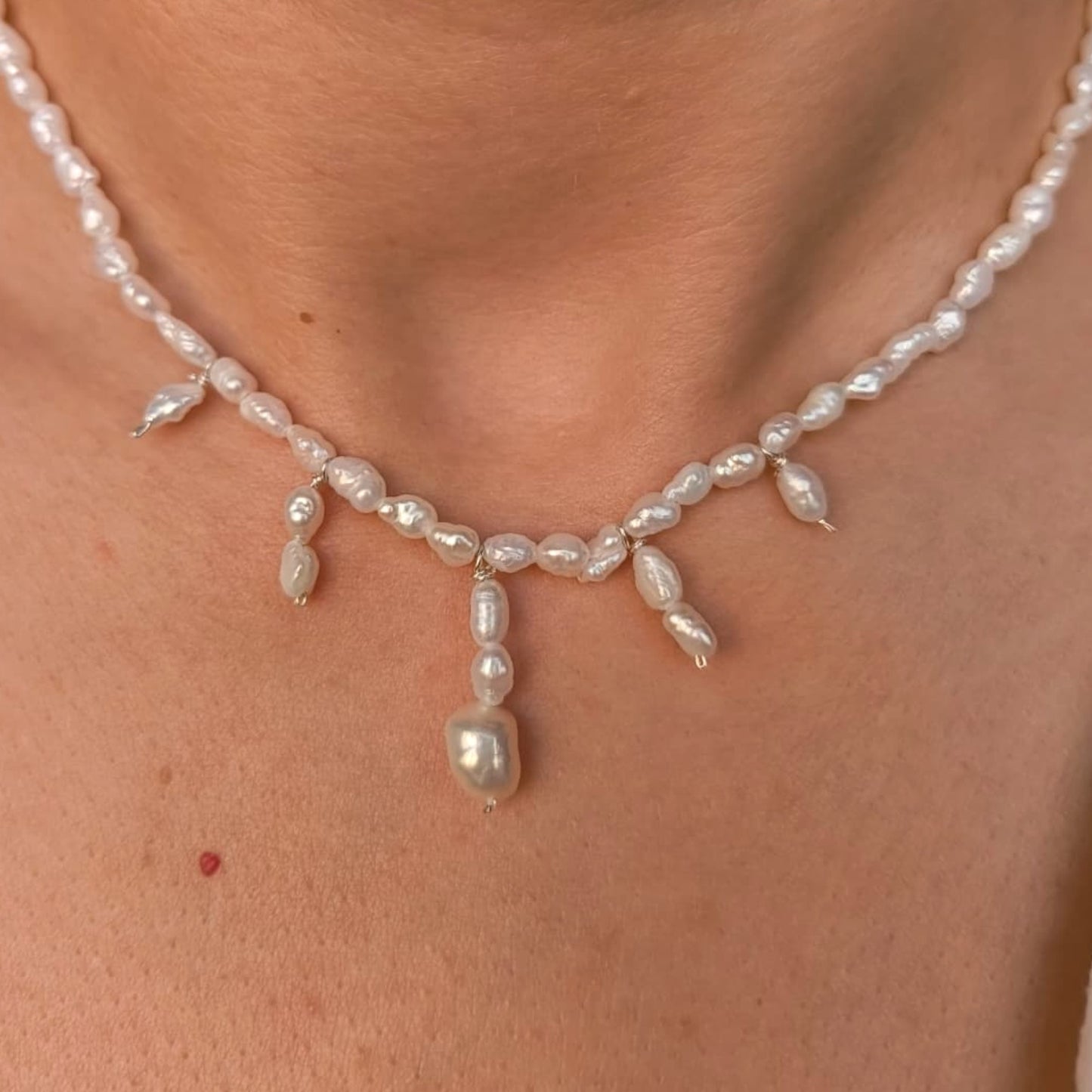 Pearl necklace worn by a person on a plain background