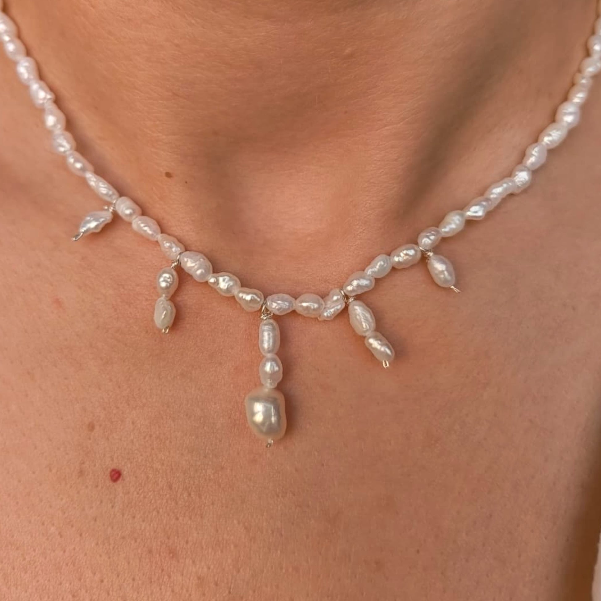 Pearl necklace worn by a person on a plain background