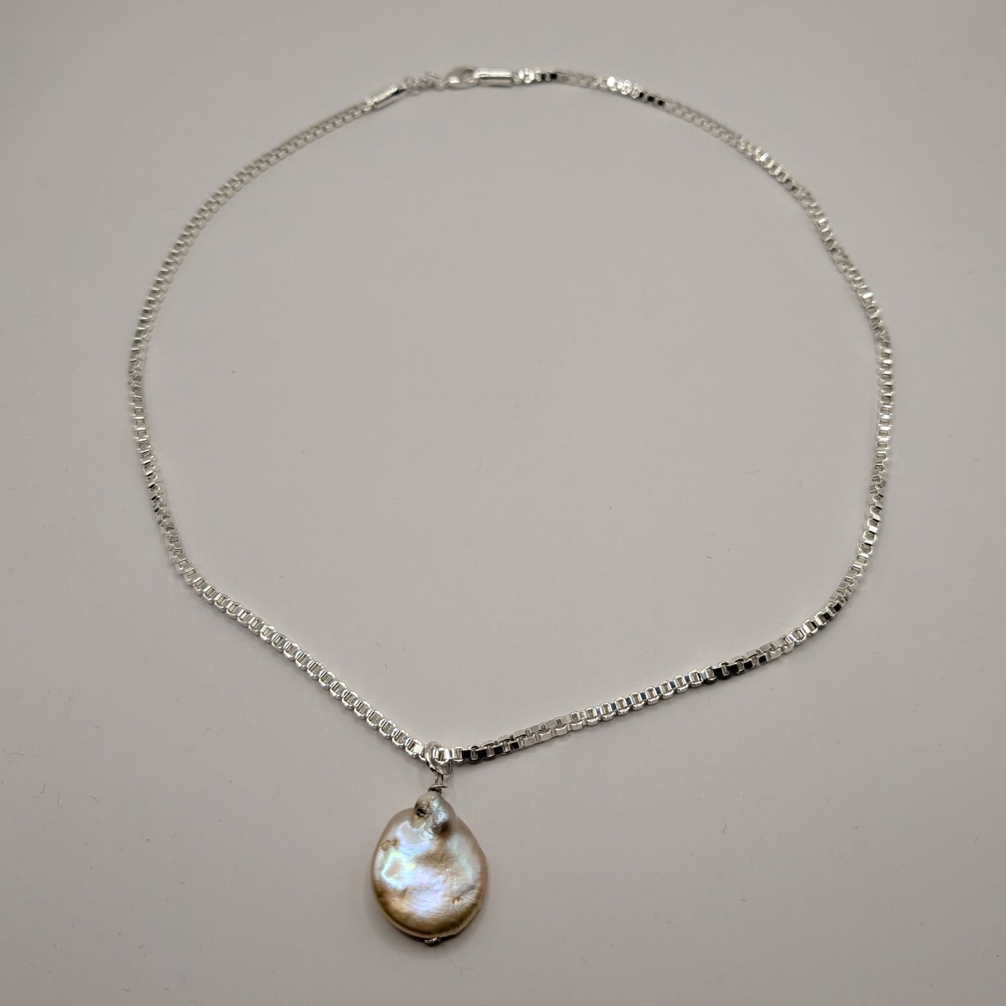Silver necklace with a teardrop-shaped pendant on a gray background