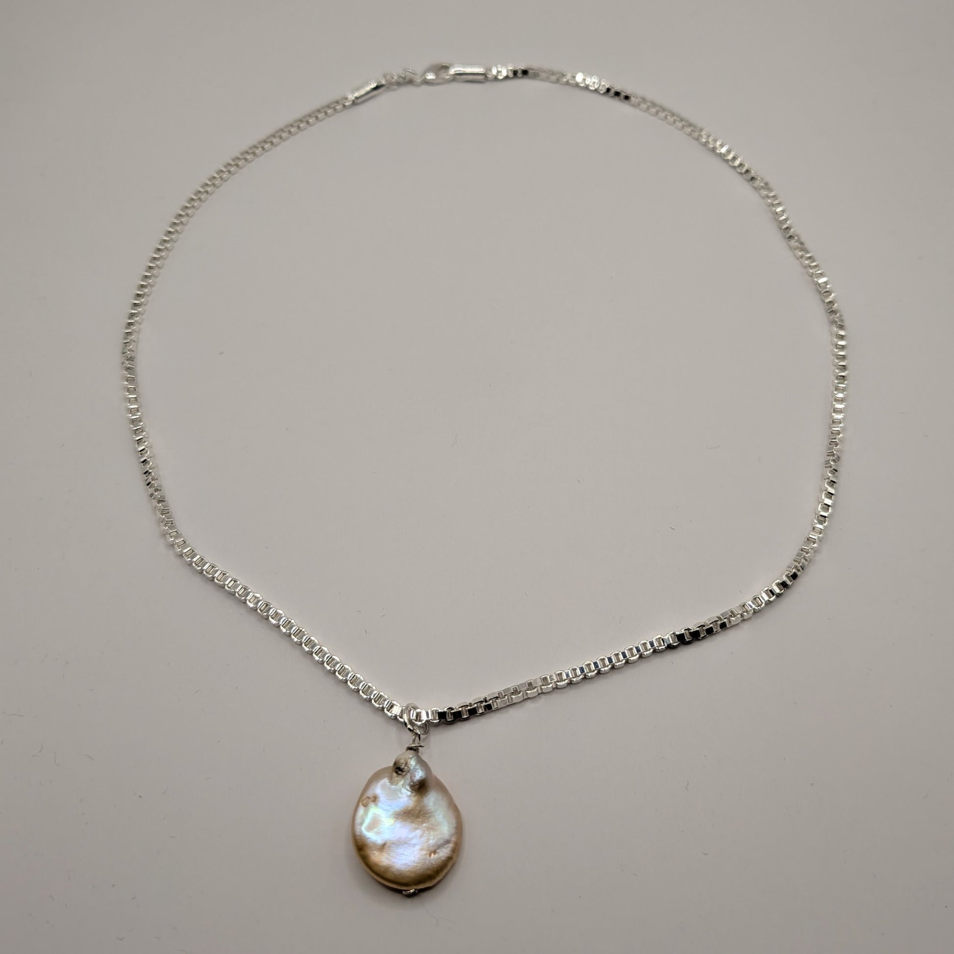 Silver necklace with a teardrop-shaped pendant on a gray background