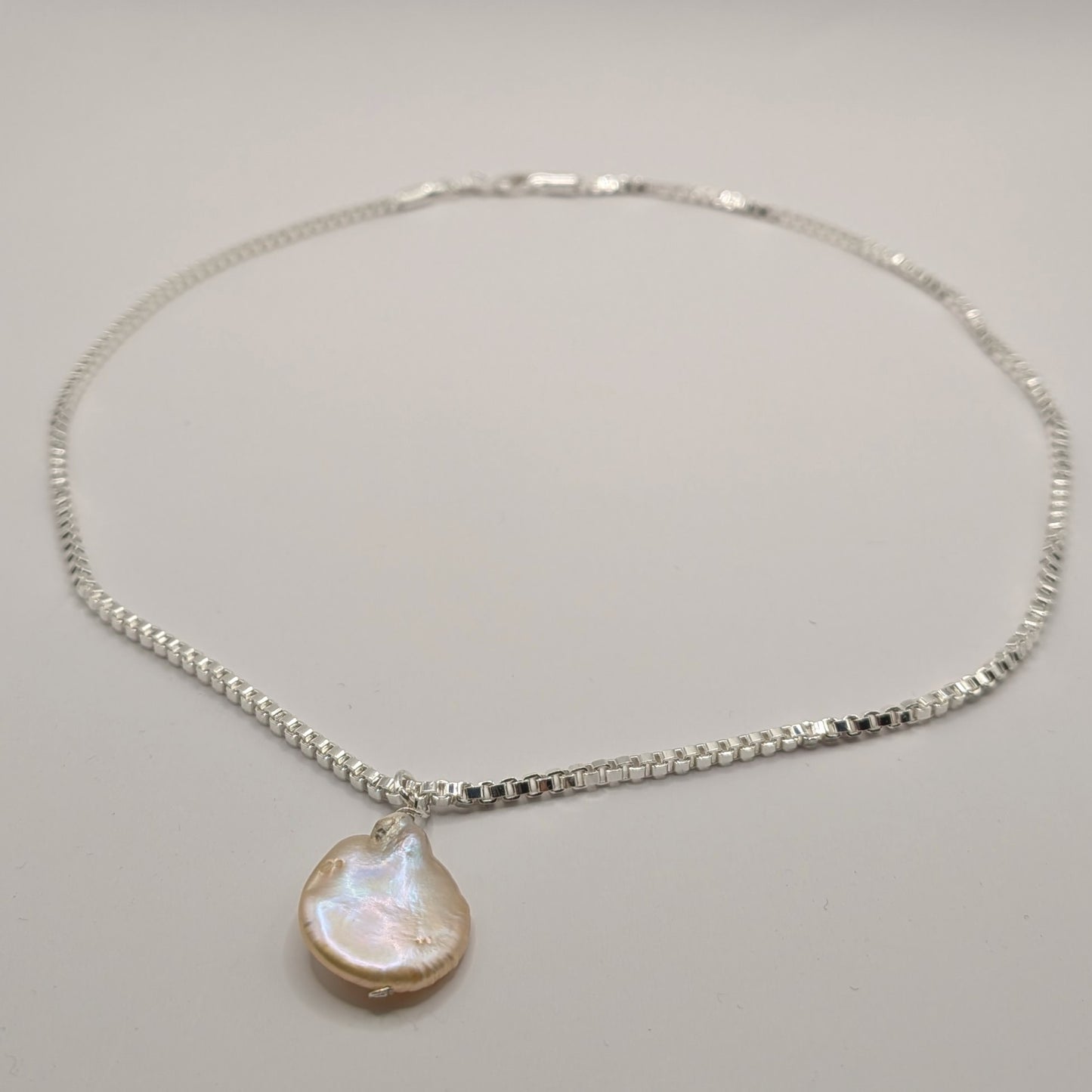 Silver necklace with a pearl pendant on a gray background