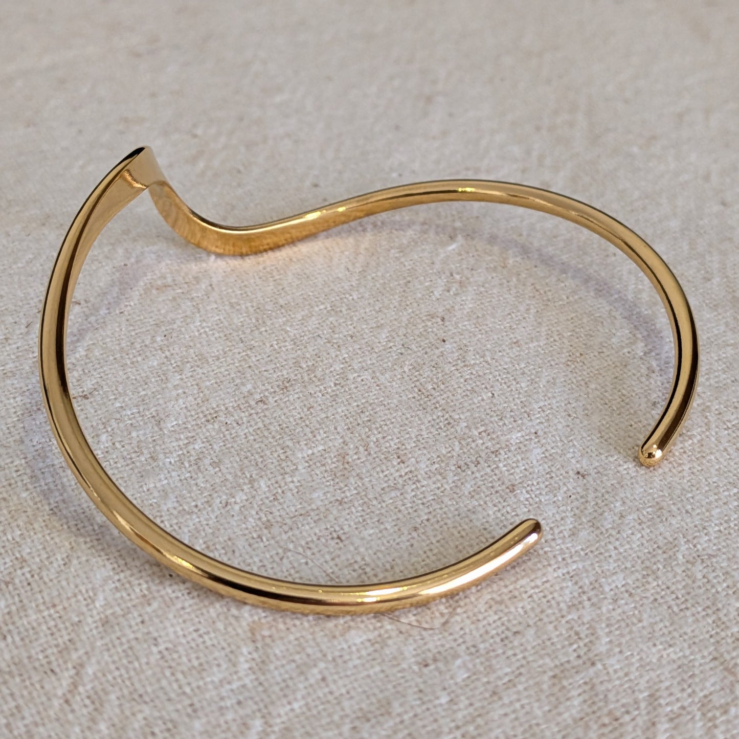 18k Gold Plated bangle on a textured beige surface