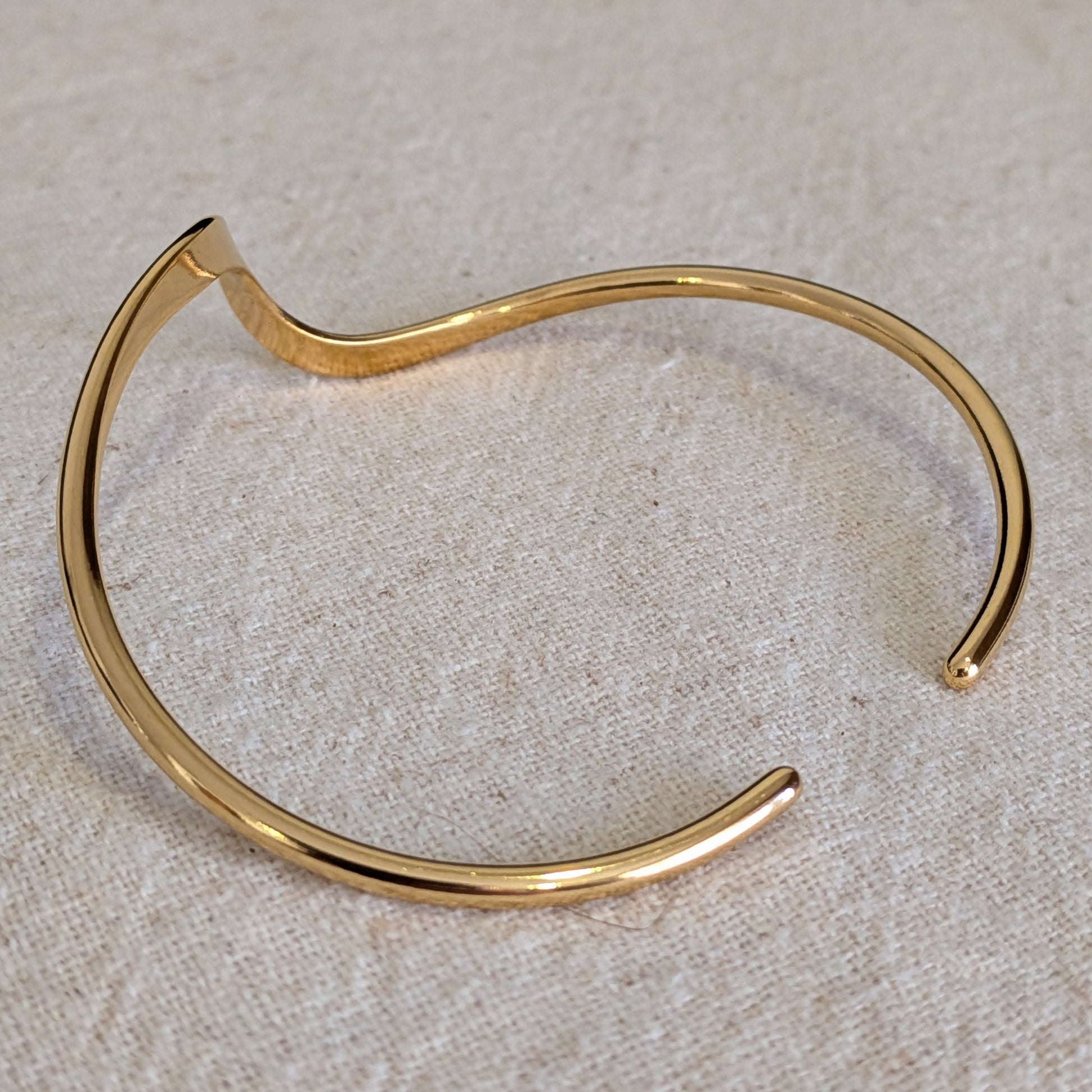 18k Gold Plated bangle on a textured beige surface