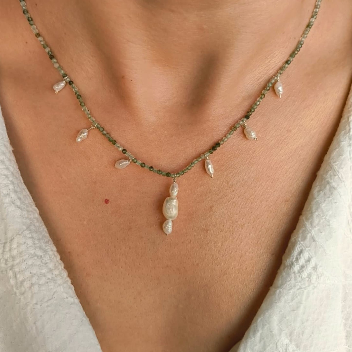Necklace with pearls on a person's neck against a neutral background