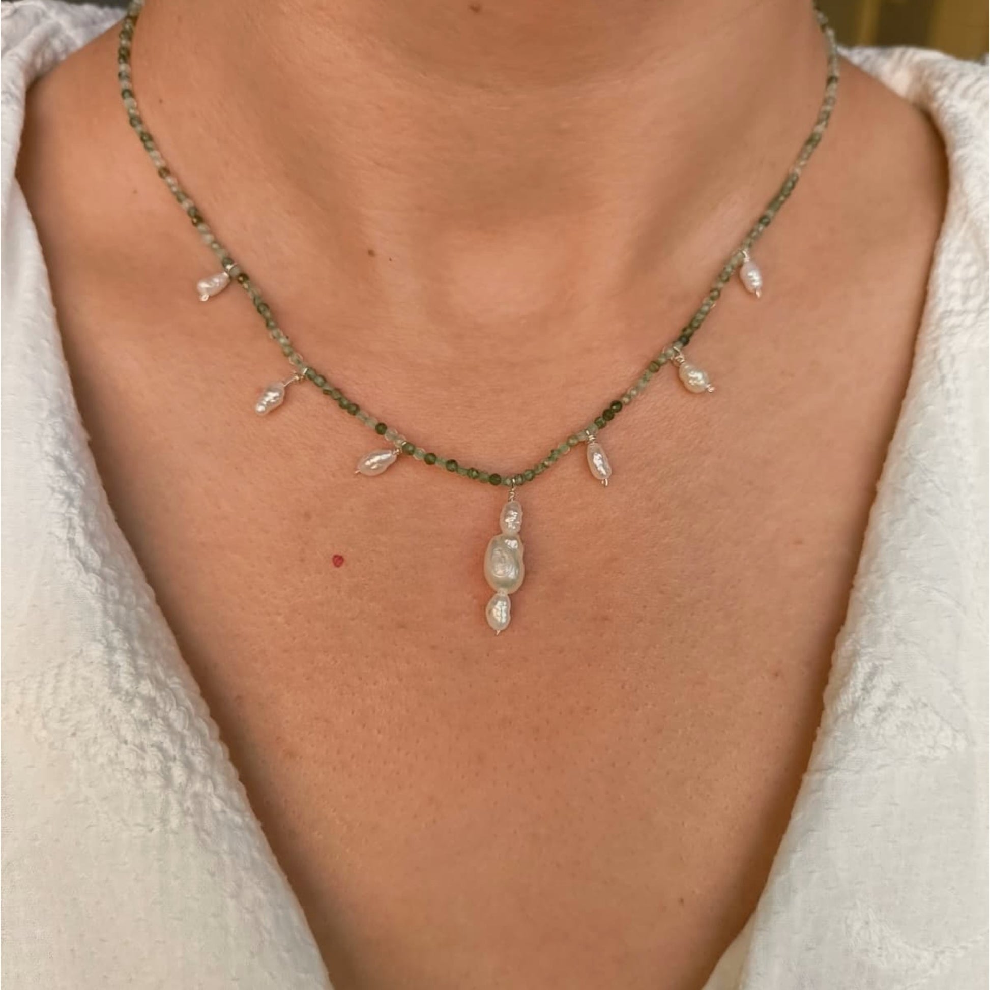 Necklace with green beads and a pendant on a person wearing a white garment.