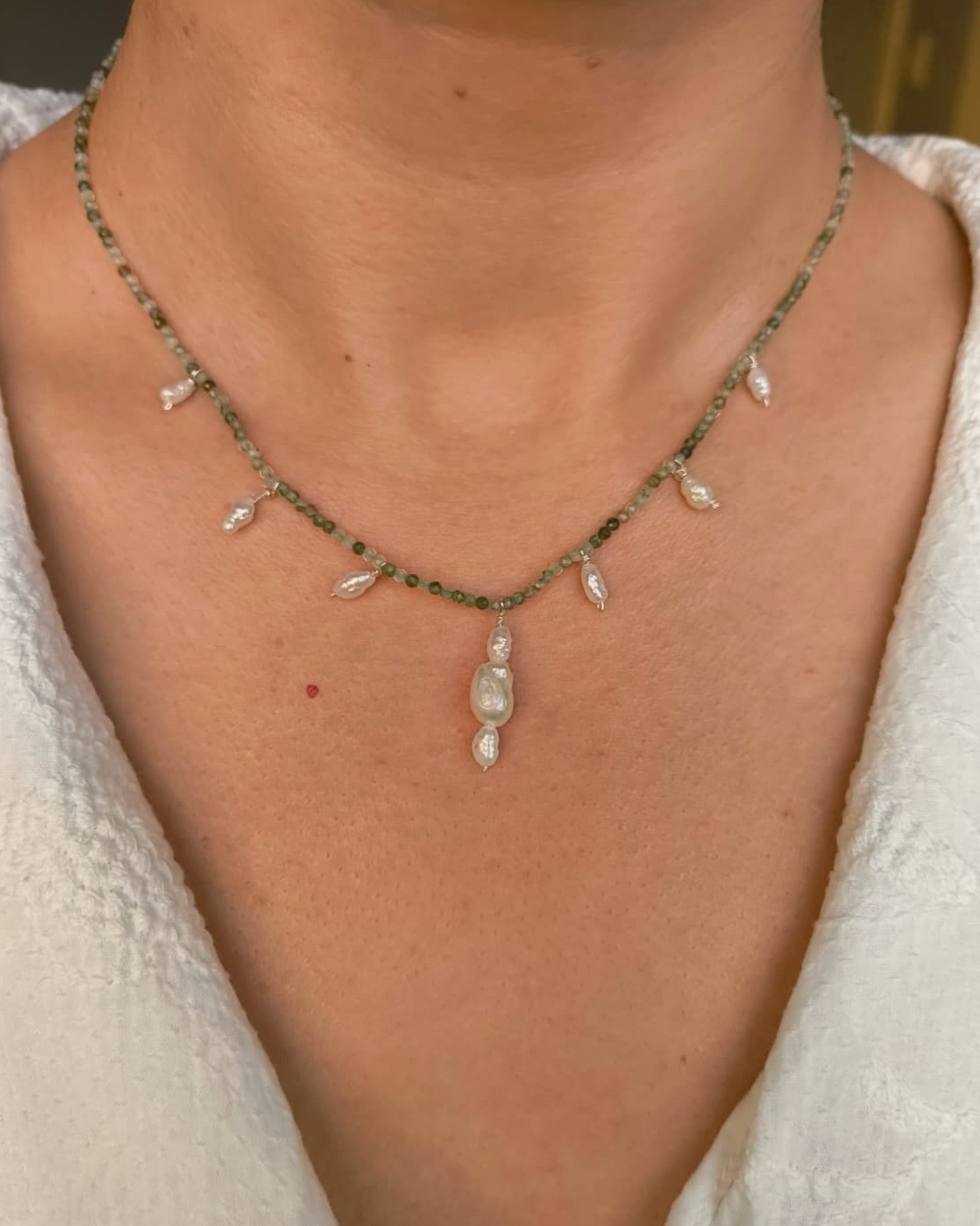 Necklace with green beads and a pendant on a person wearing a white top.