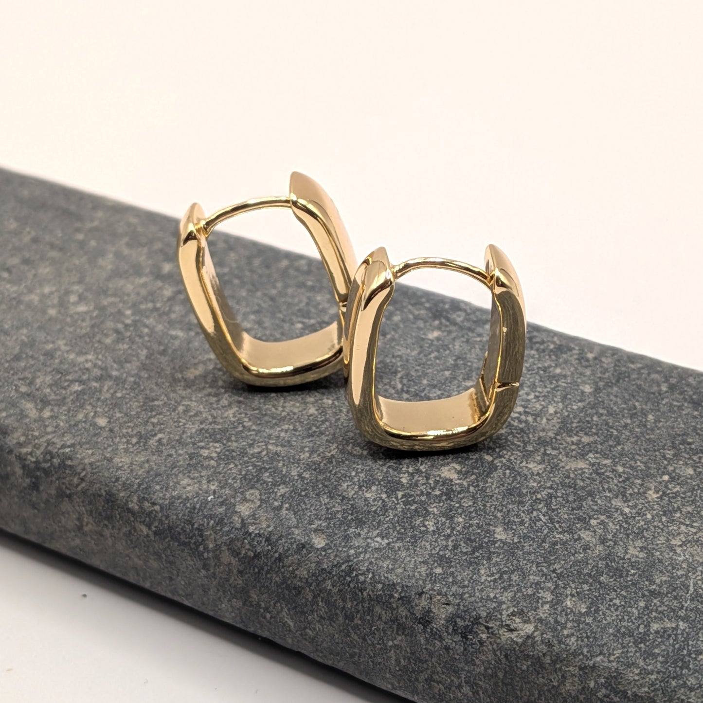 Gold hoop earrings on a gray stone surface