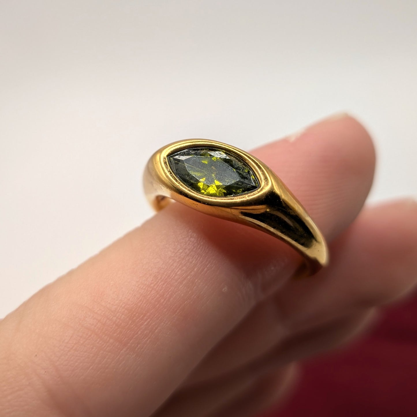 Gold ring with a green gemstone on a finger against a white background