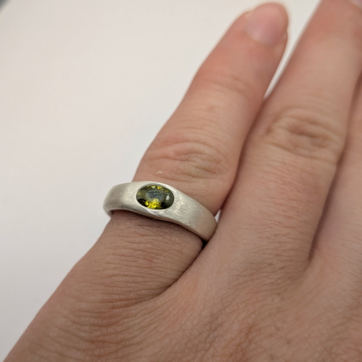 A close-up of a hand wearing a rustic silver ring with an oval green gemstone.