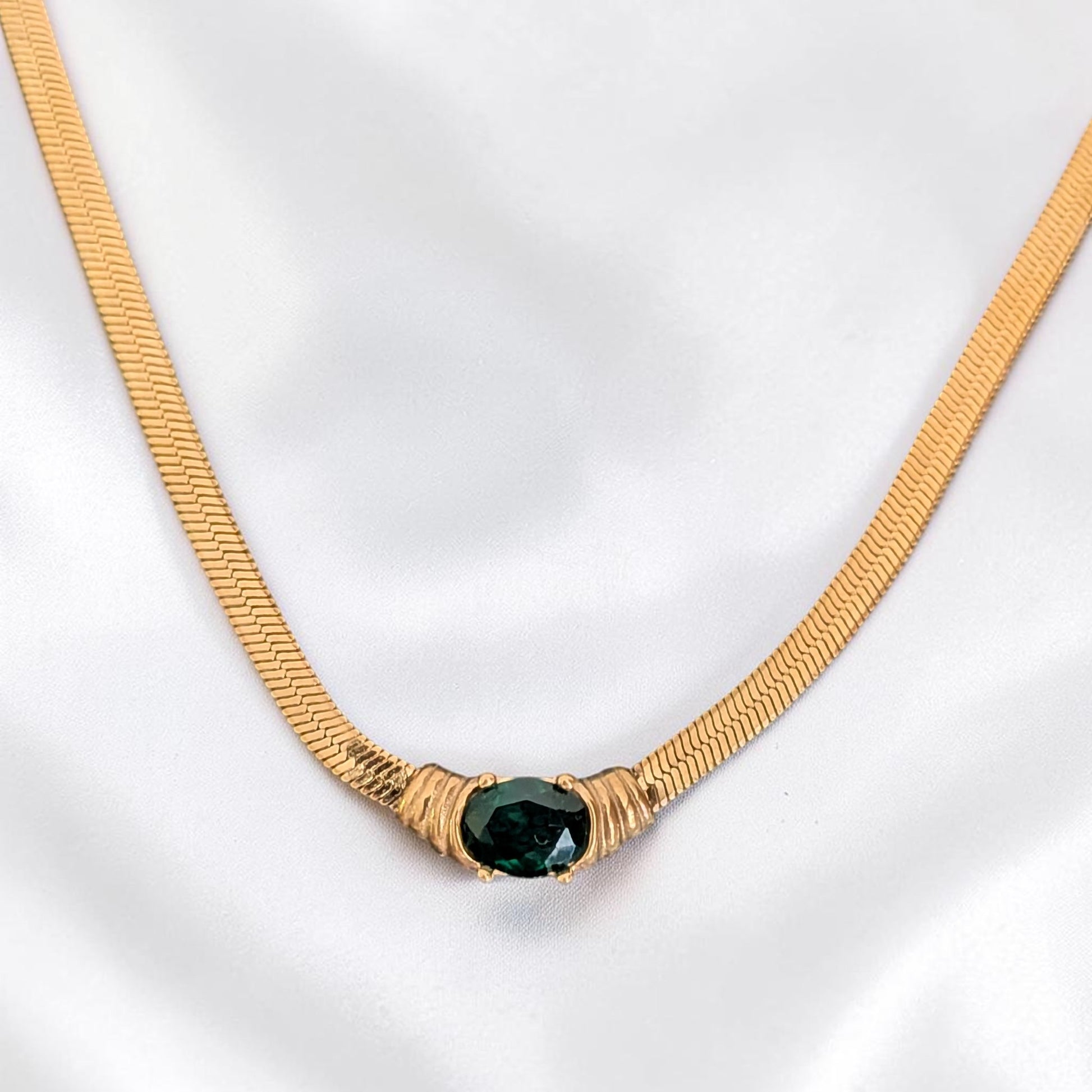 Gold necklace with a green gemstone on a white background