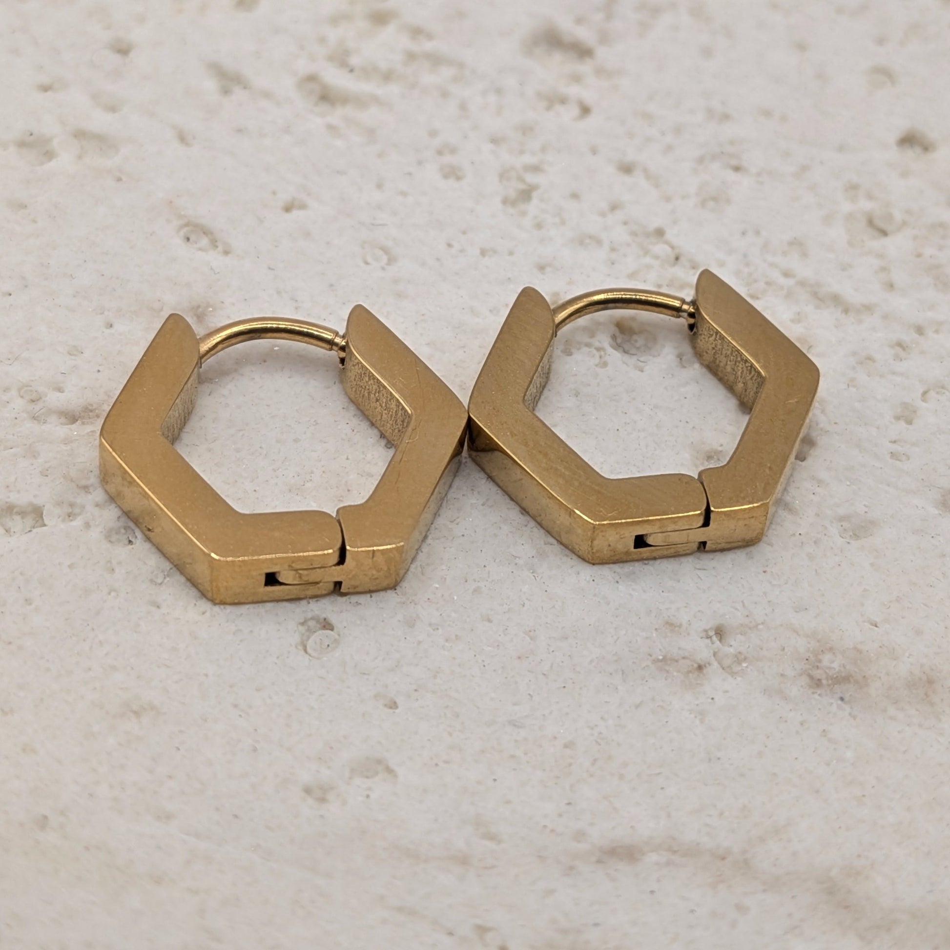 Pair of gold hexagonal hoop earrings on a light marble surface
