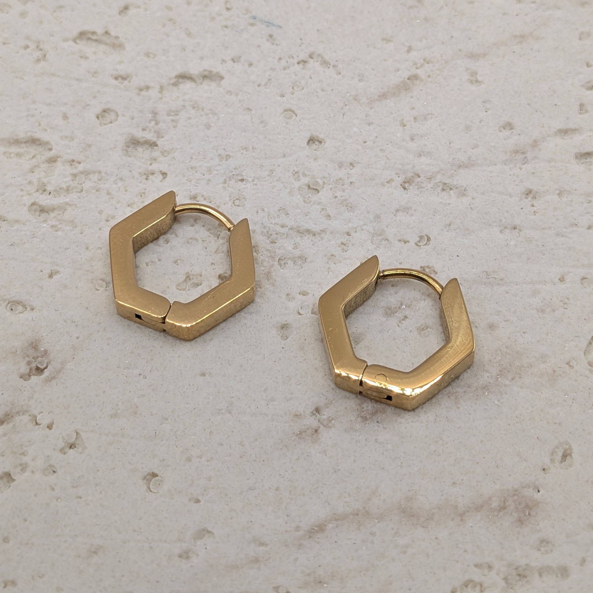 Gold hexagonal hoop earrings on a light stone surface