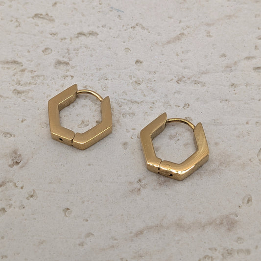 Gold hexagonal hoop earrings on a light stone surface