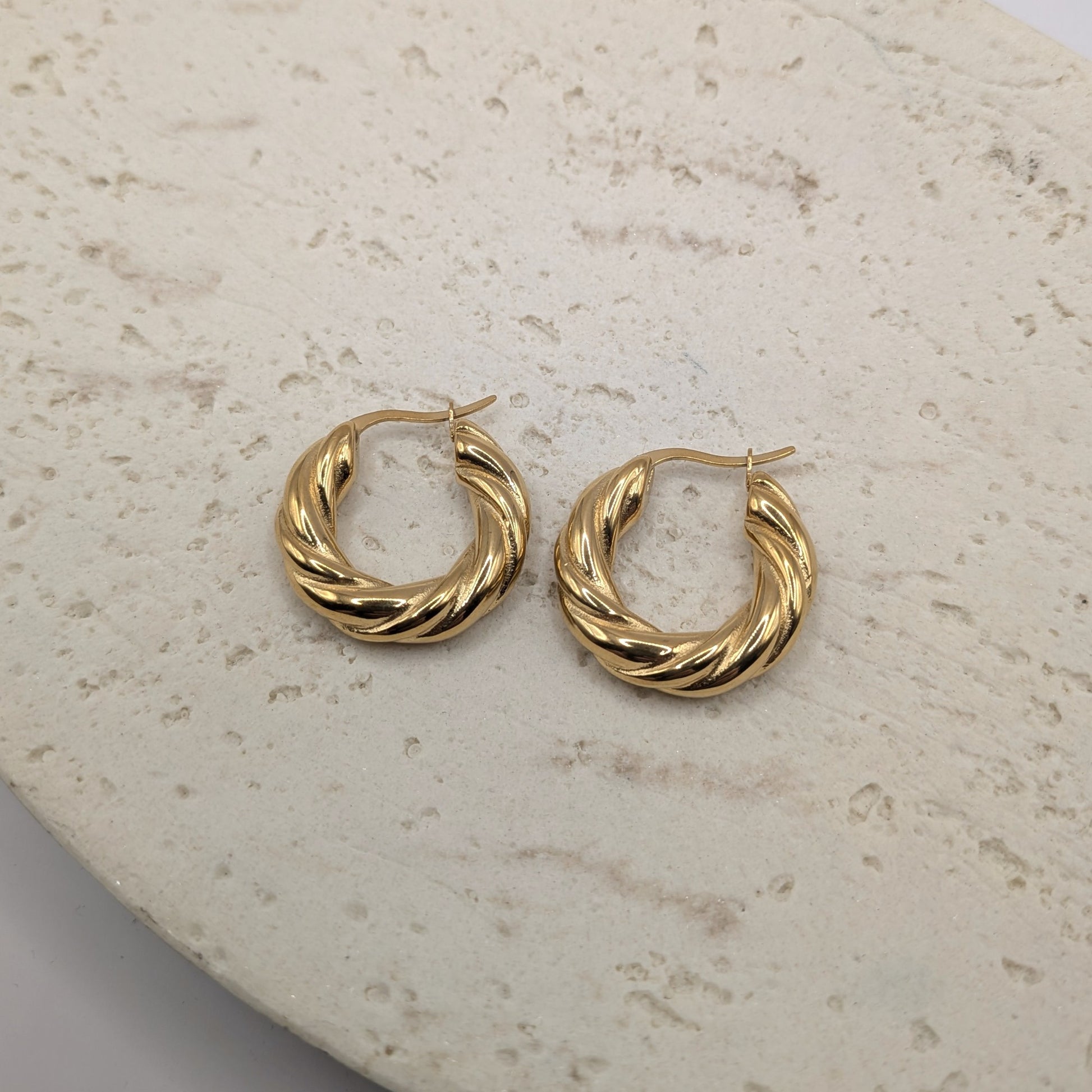 Pair of gold hoop earrings on a textured beige surface