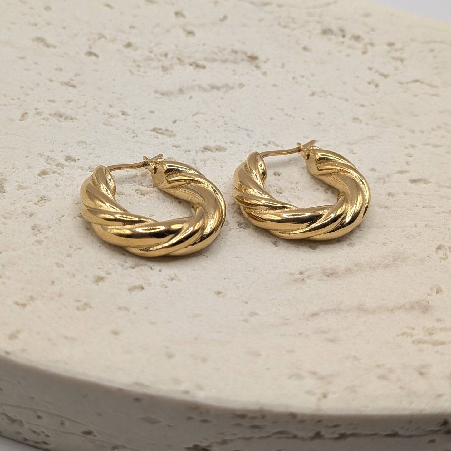 Pair of gold hoop earrings on a light stone surface
