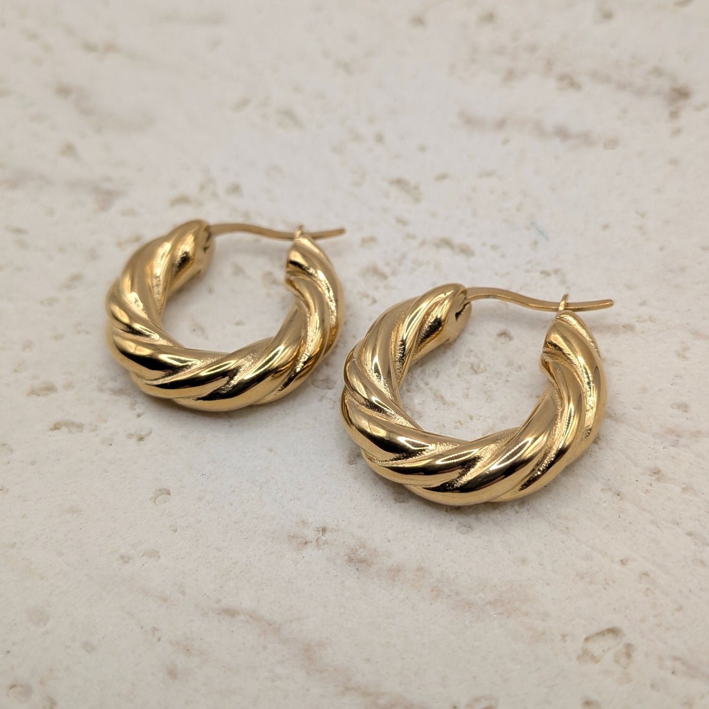 Gold hoop earrings on a light marble background