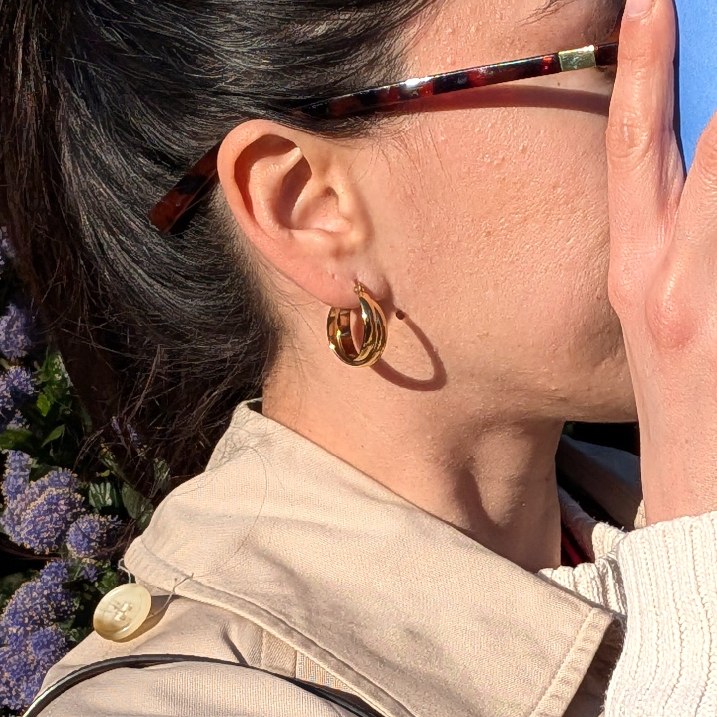 Close-up of a person wearing gold hoop earrings with a blurred background