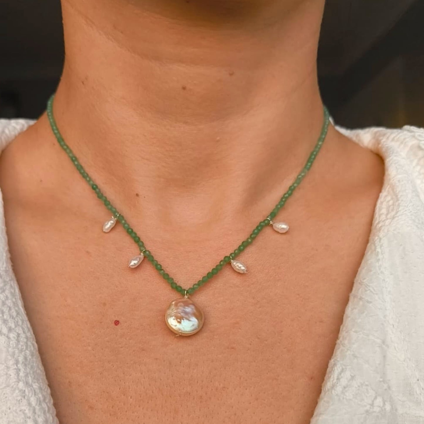 Close-up of a green beaded necklace with a pendant on a person wearing a white top.