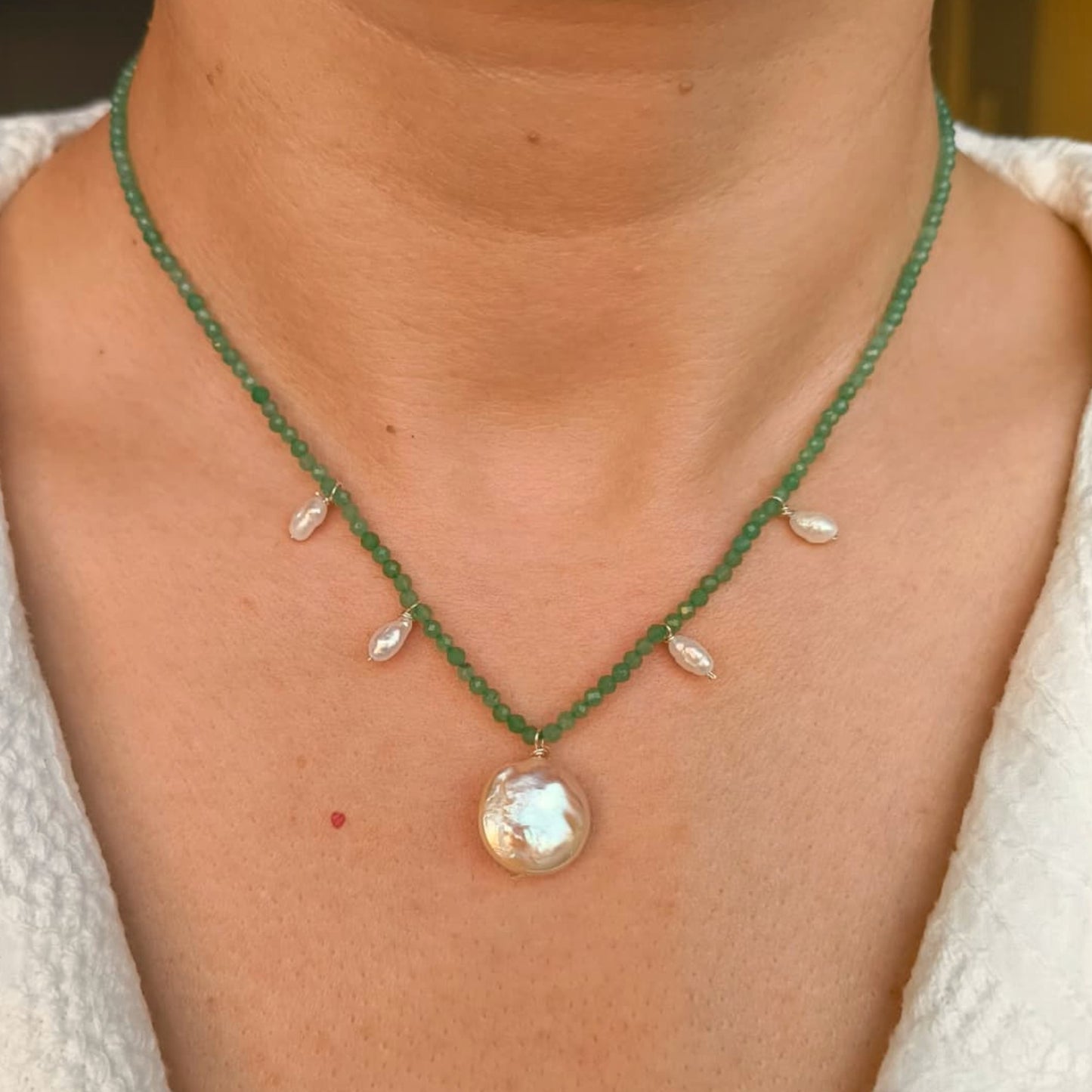 Green beaded necklace with a large pearl pendant on a person wearing a white top.
