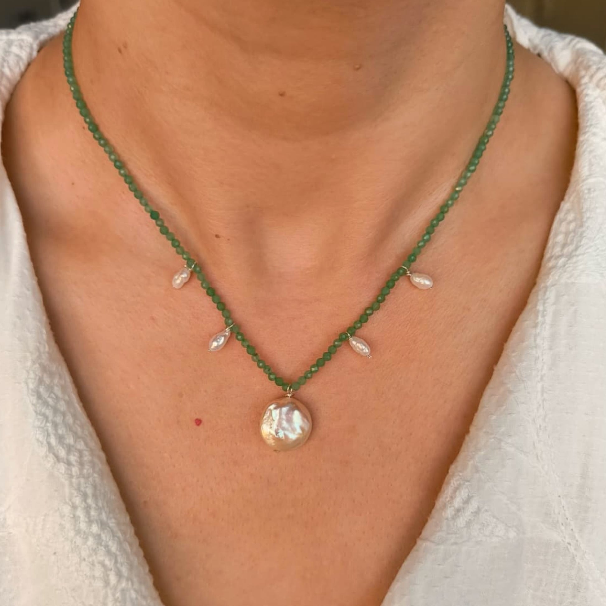 Green beaded necklace with a pearl pendant worn by a person