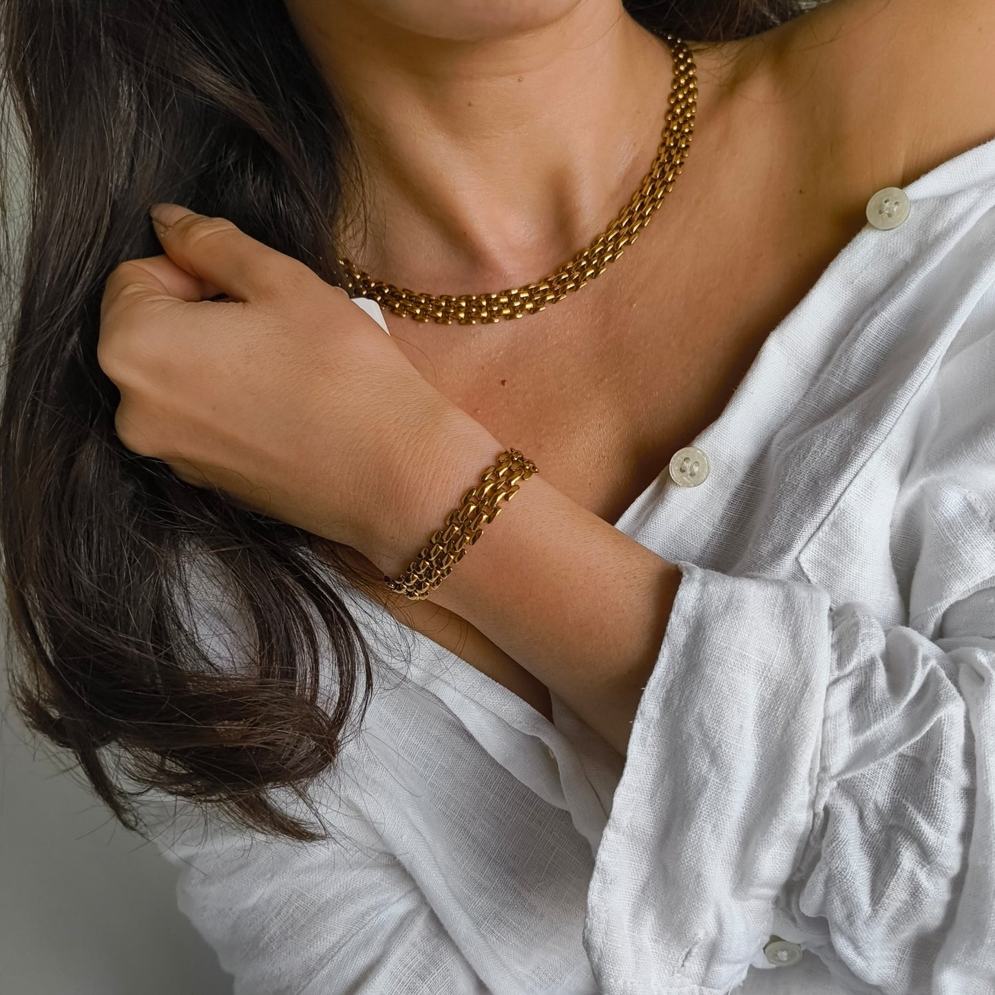 Person wearing a gold chain necklace and bracelet, with a white shirt.